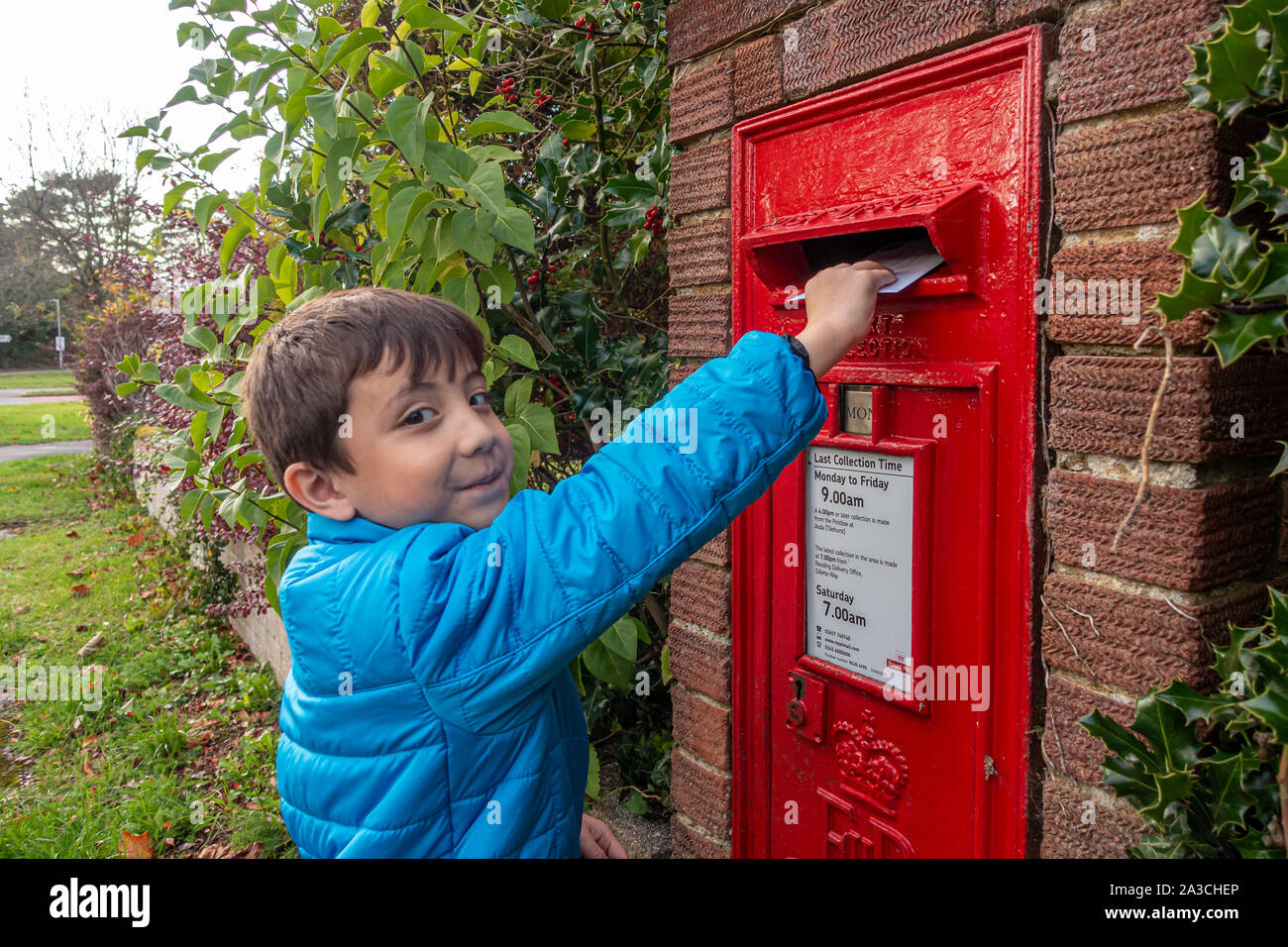 A young boy posts a letter in a post box built into a wall. Stock Photo