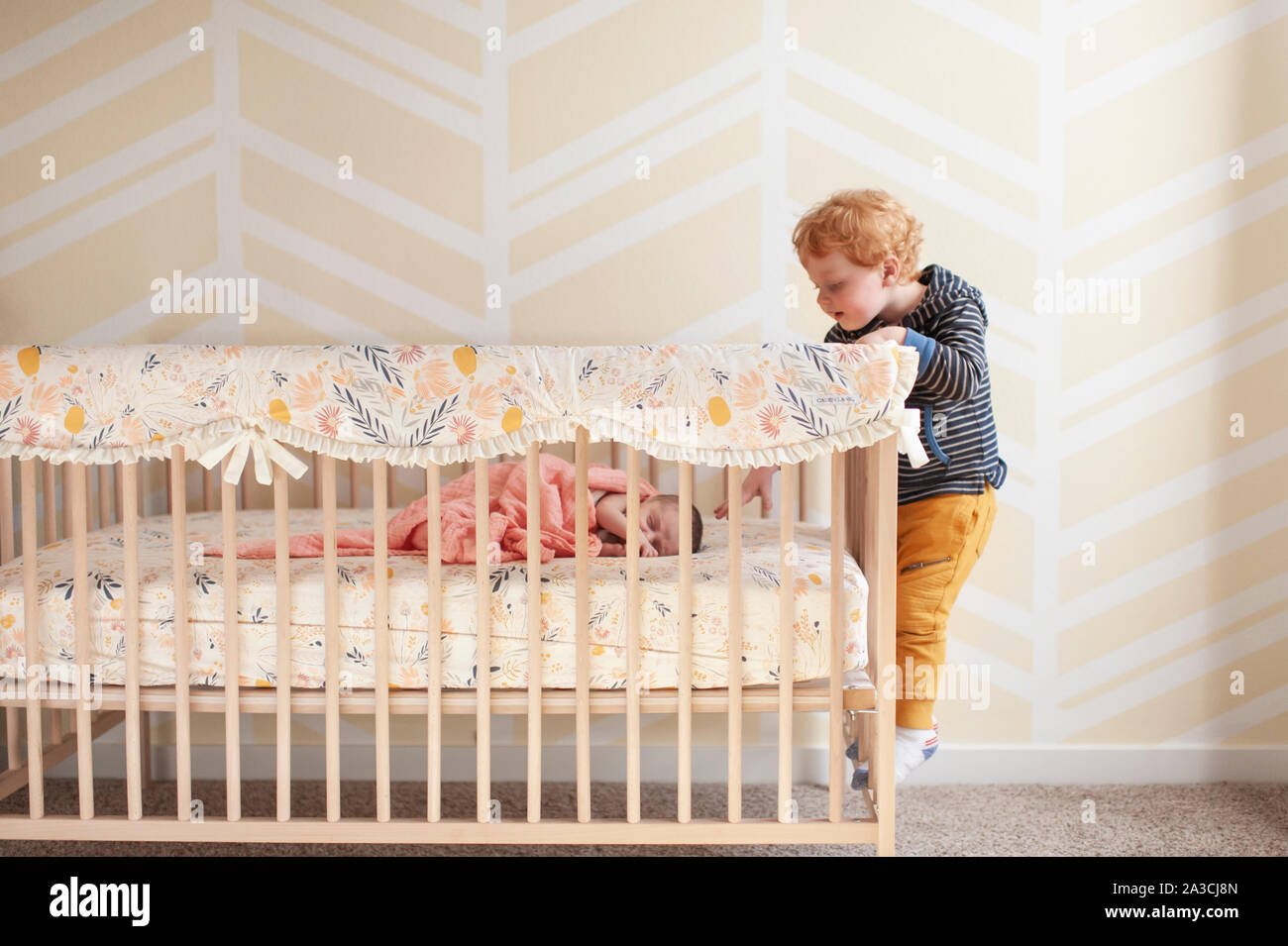 Toddler reaching in crib trying to touch newborn baby's head Stock Photo Alamy