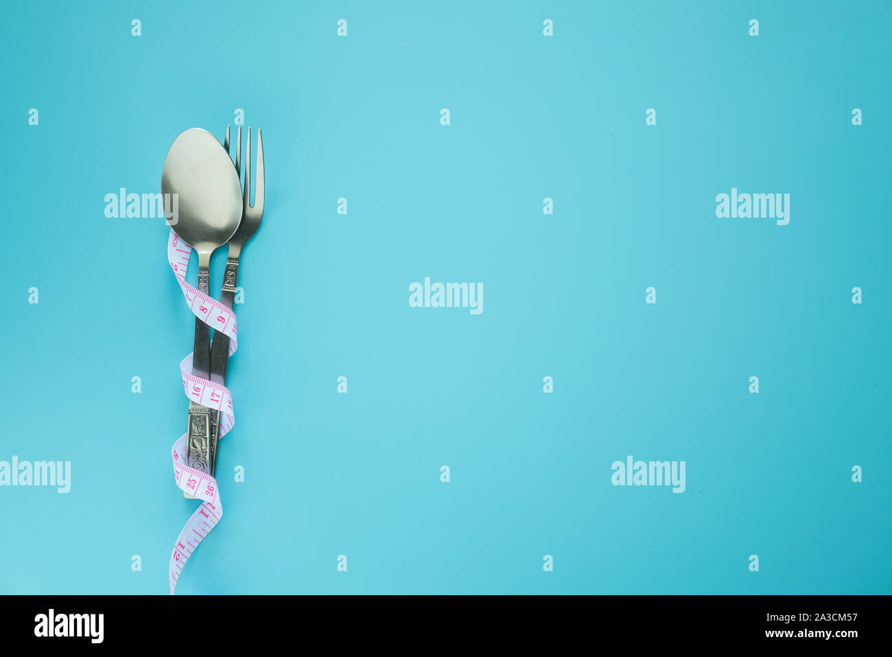 spoon and fork wrapped in measuring tape isolated on blue background with copy space. diet , food control and weight loss concept. Stock Photo