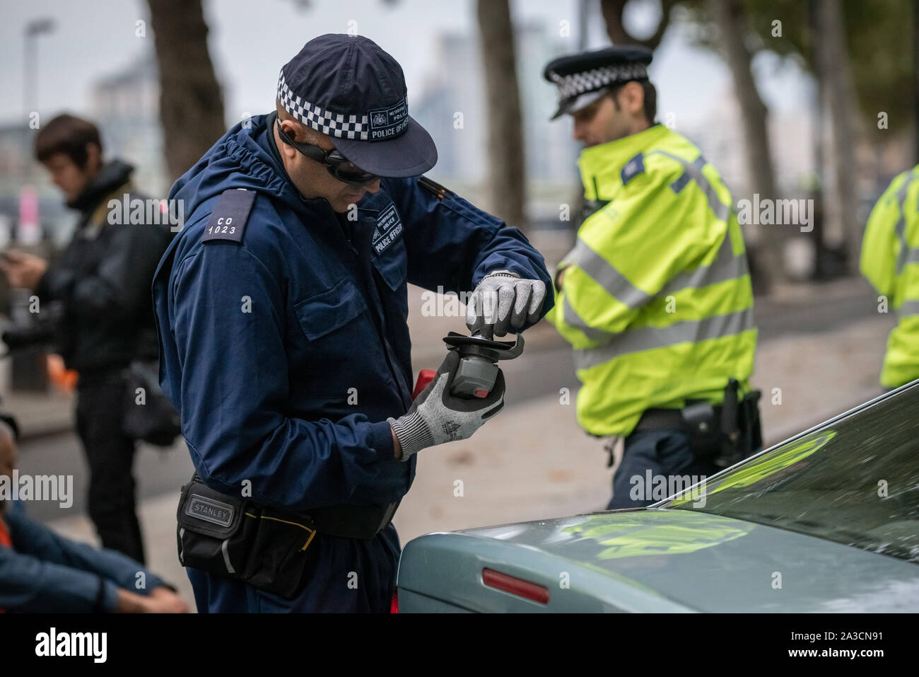 Specialist police unit attempt to cut free a locked-on protester from inside a car parked to obstruct Victoria Embankment which the Extinction Rebellion protesters attempted to occupy from 6am. The environmental campaigners begin a new wave of protest action this morning causing disruption in London. Forces across England have been asked to contribute specialist “protest removal teams” trained and equipped to deal with protesters using locks and glue to hamper efforts their removal as they attempt to block key routes. Stock Photo