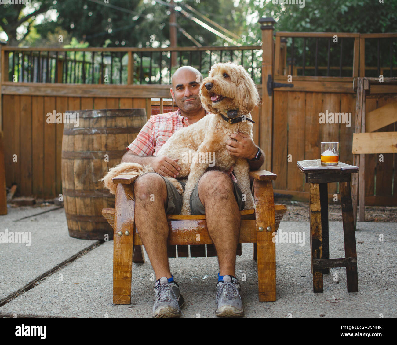 A man sits on a handmade wooden chair with a happy dog on his lap Stock Photo