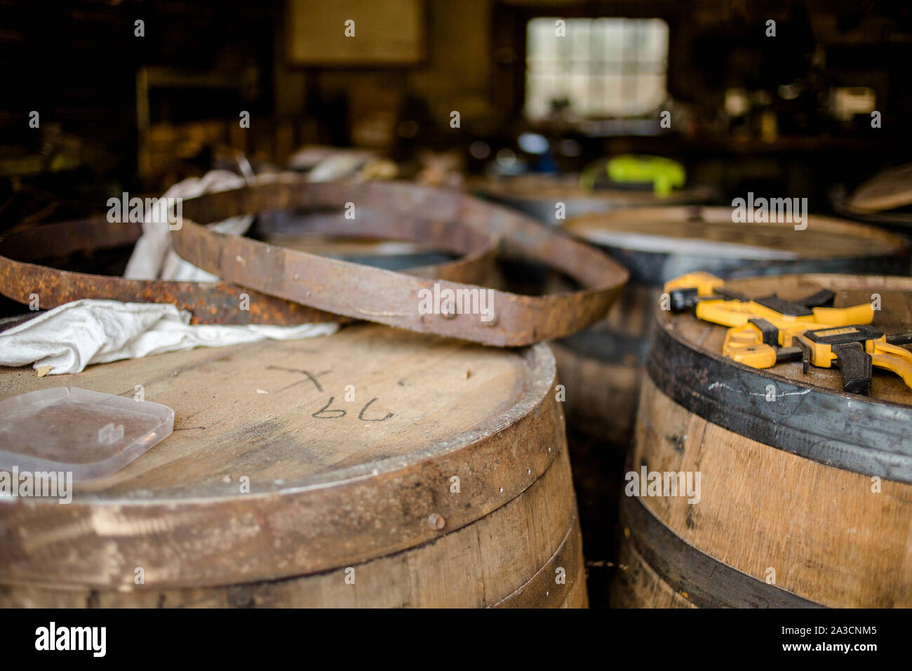 A line of bourbon barrels stand in a workshop with tools on top Stock Photo