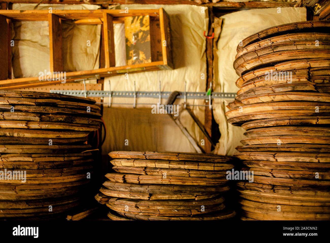 Stacks of wood bourbon barrel lids lean on  wall lined with tools Stock Photo