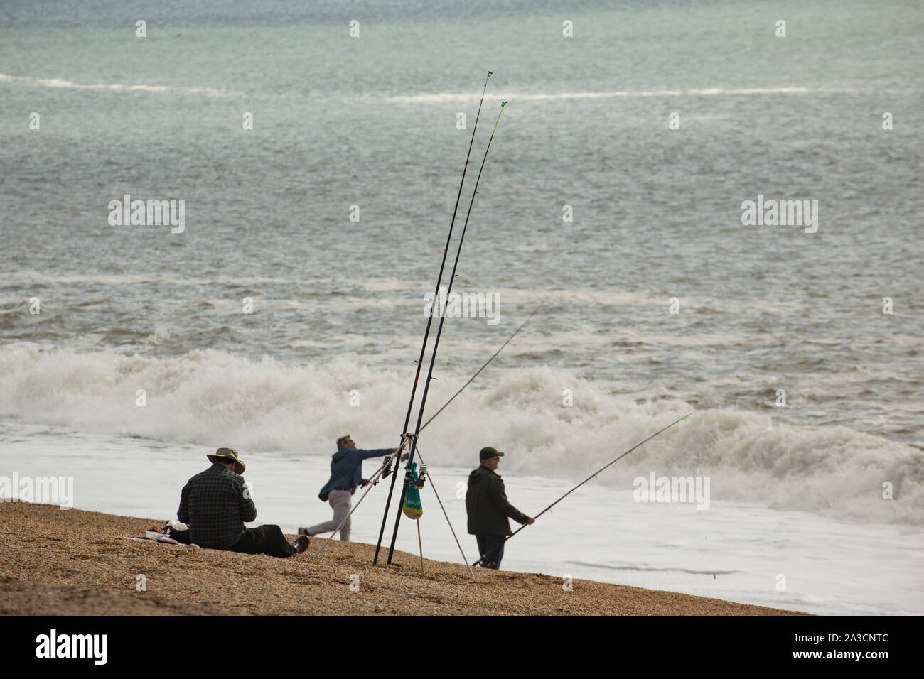 Anglers fishing on Chesil beach in October the day after a storm when the wind has dropped. Fishing after a storm can be productive as fish such as co Stock Photo