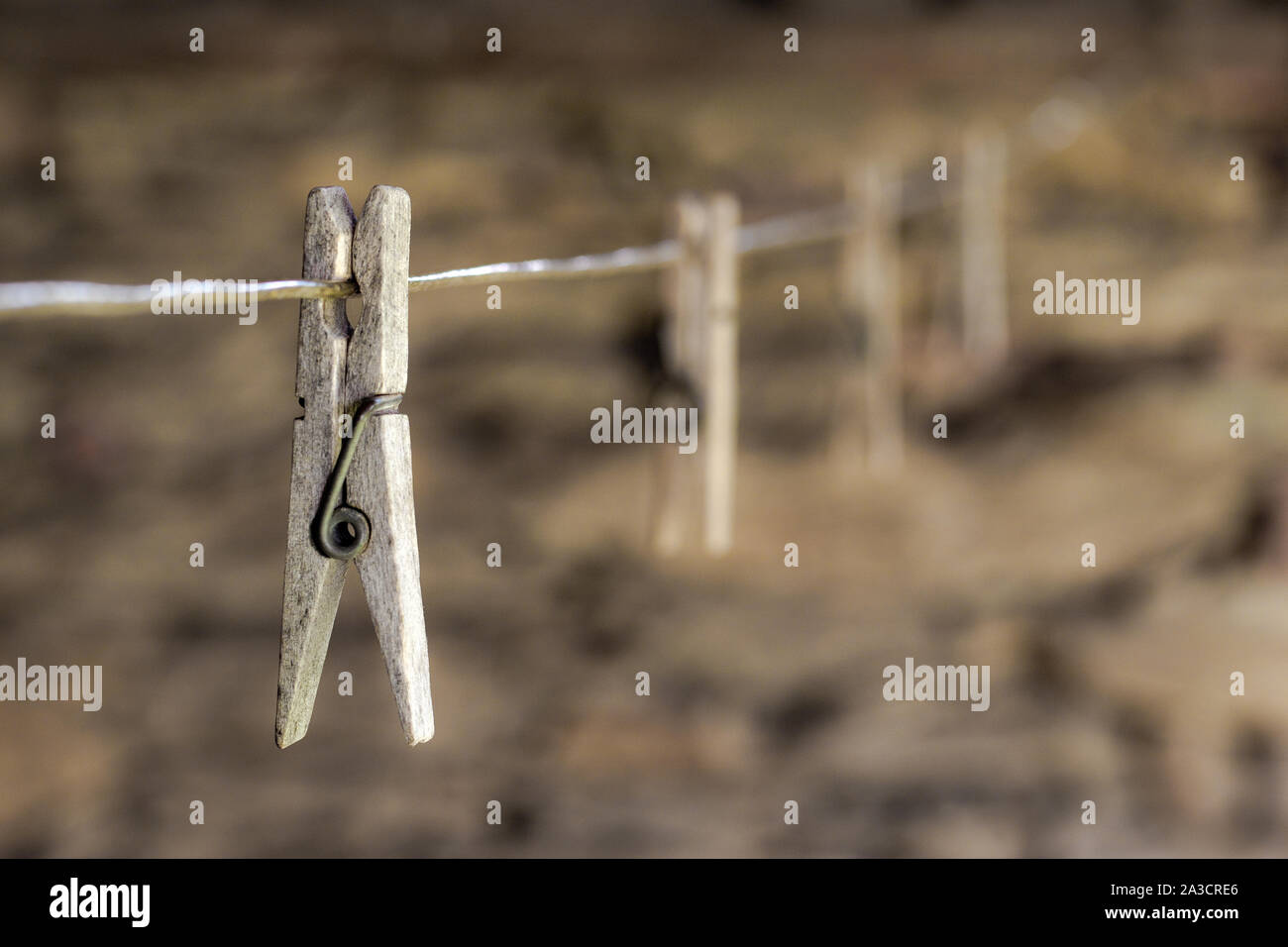 Old wooden clothes pegs on cord with stone wall on background Stock Photo