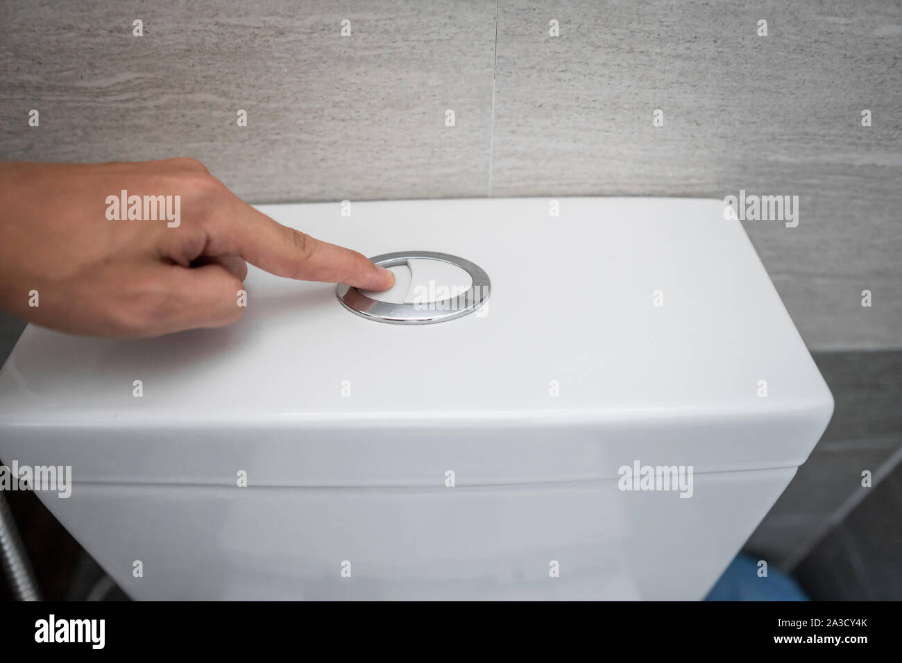 Close up of finger pushing a flush toilet button for cleaning a toilet. Stock Photo