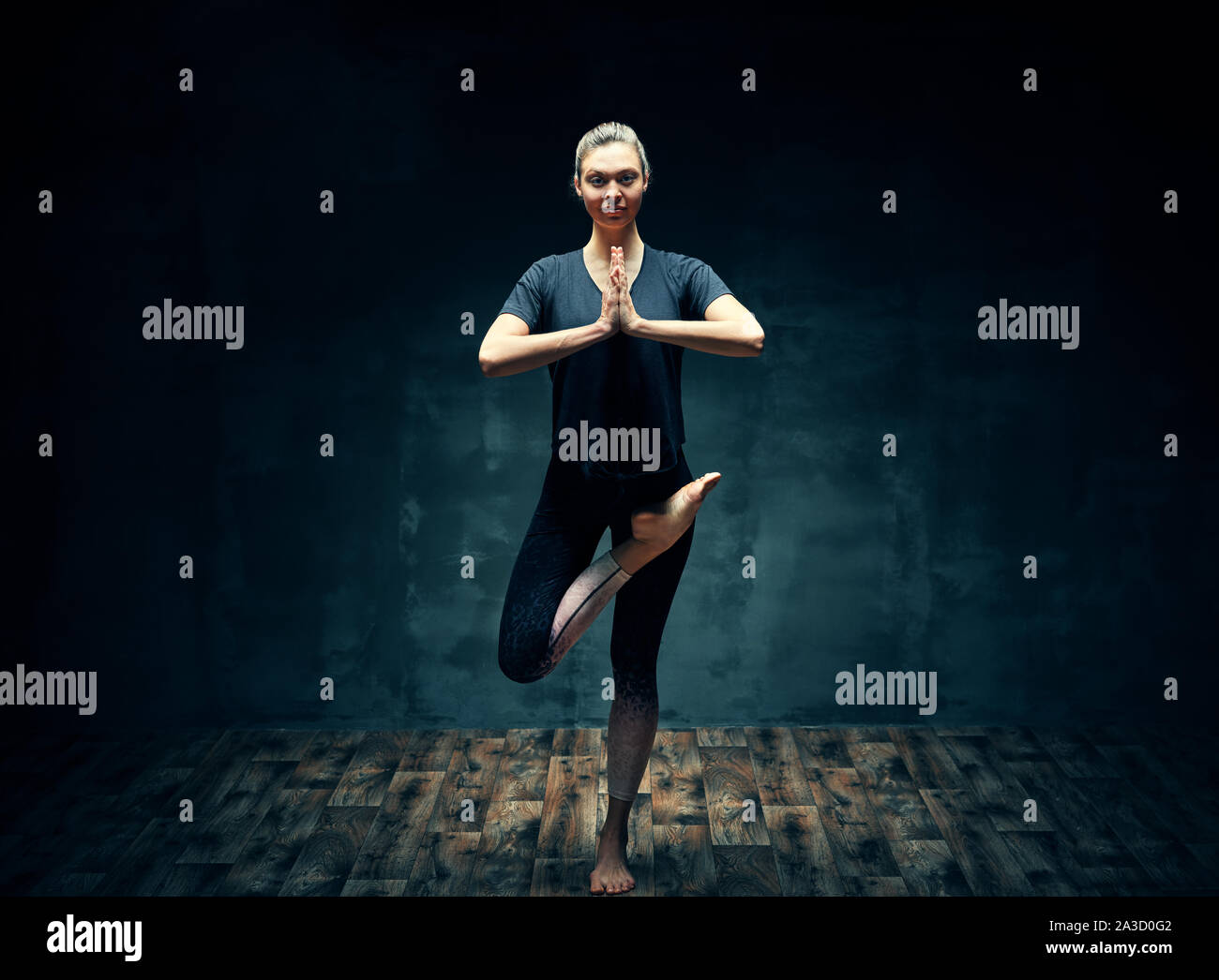 Young beautiful woman doing yoga asana half bound lotus tree pose in dark room. Wellbeing, meditation and healthy lifestyle.  Ardha baddha padma vriks Stock Photo