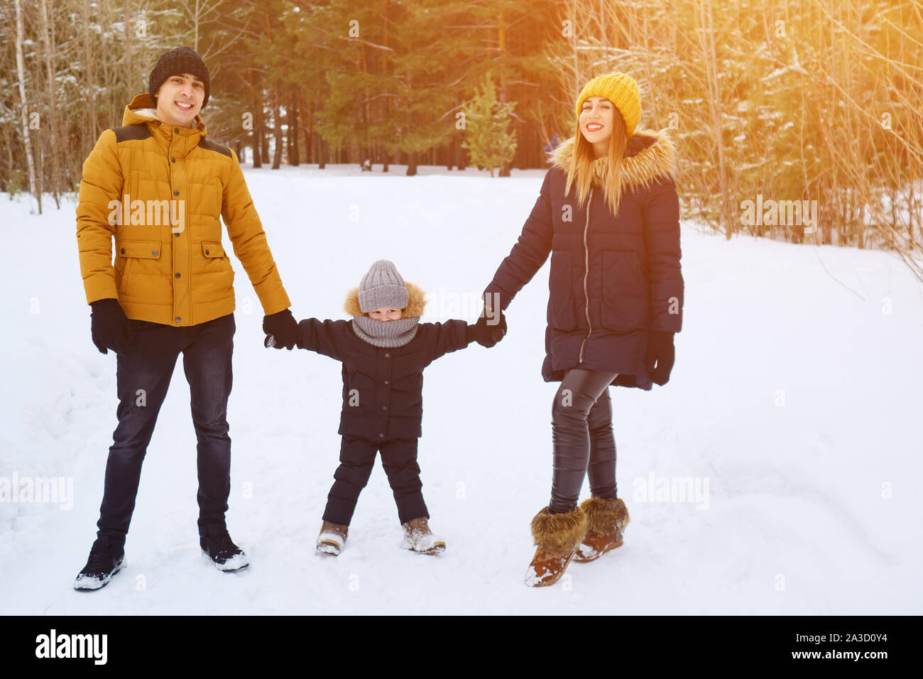 Portrait of happy family in winter day. Mom and dad are holding hands their little son in winter park. Family lovely moments. Stock Photo