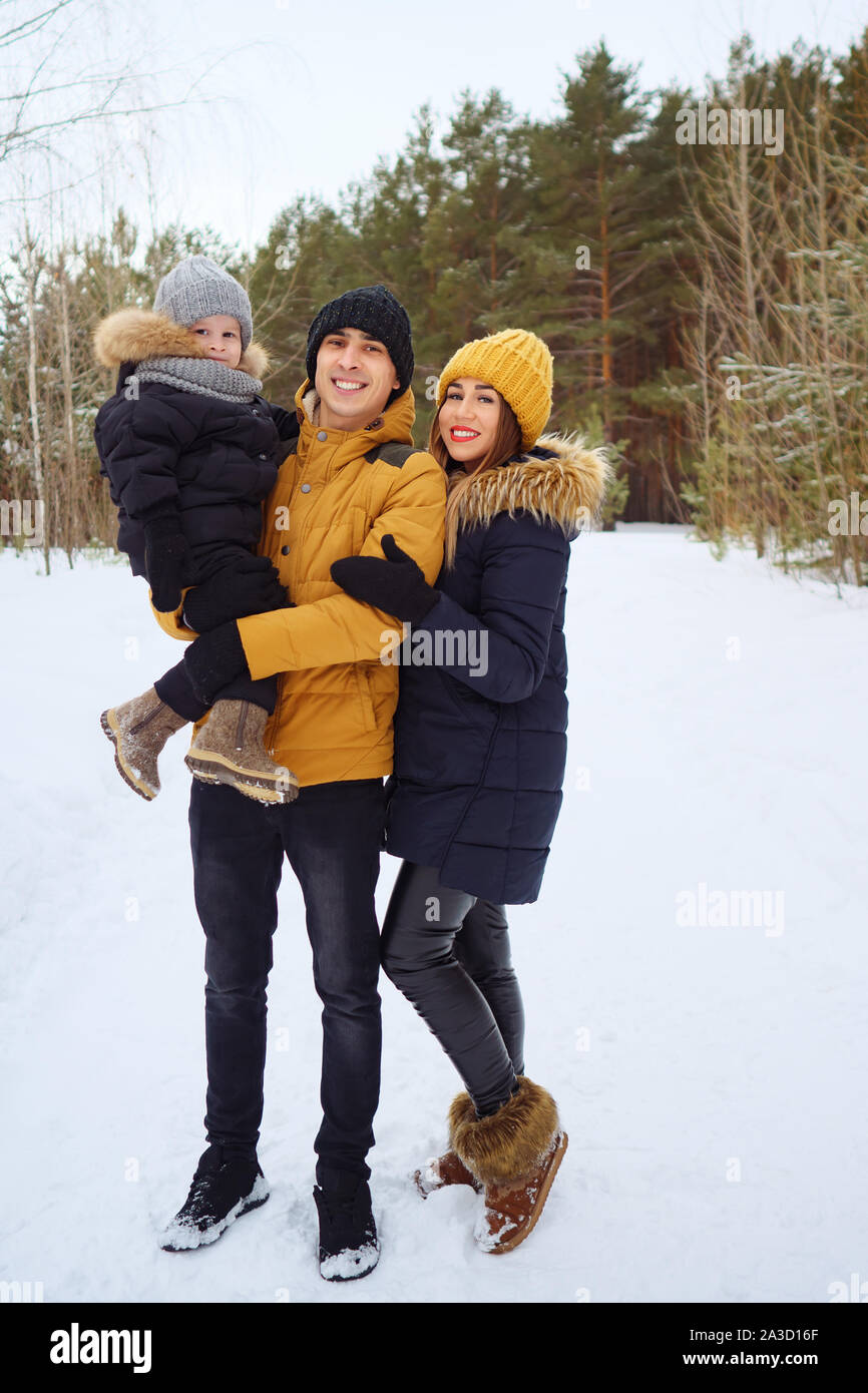 Portrait of happy family in winter day looking at camera. Mom and dad are cuddling their little son in winter park. Family lovely moments. Stock Photo