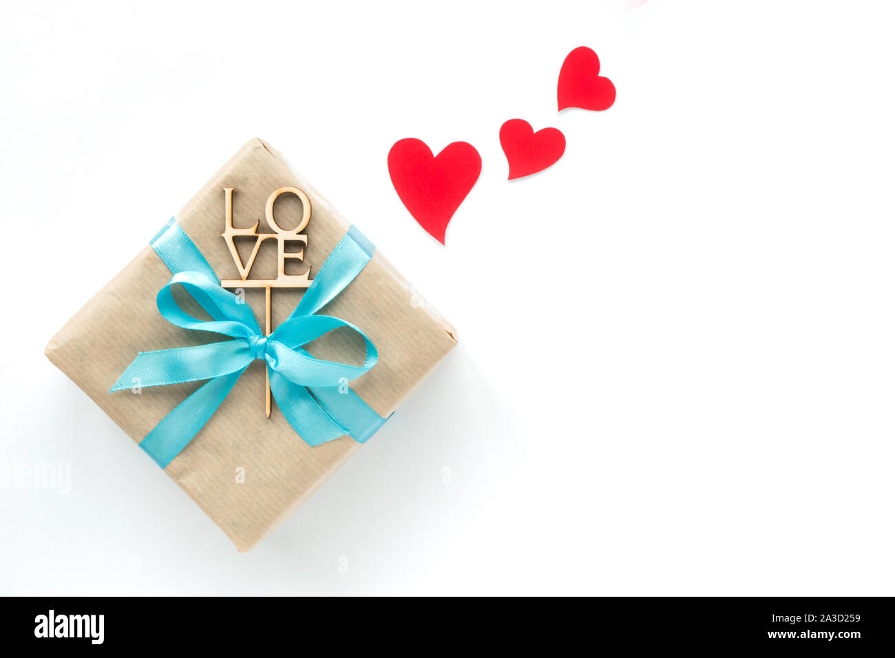 Gift box wrapped in brown paper with light blue ribbon and red hearts on white background. Top view. Copyspace Stock Photo