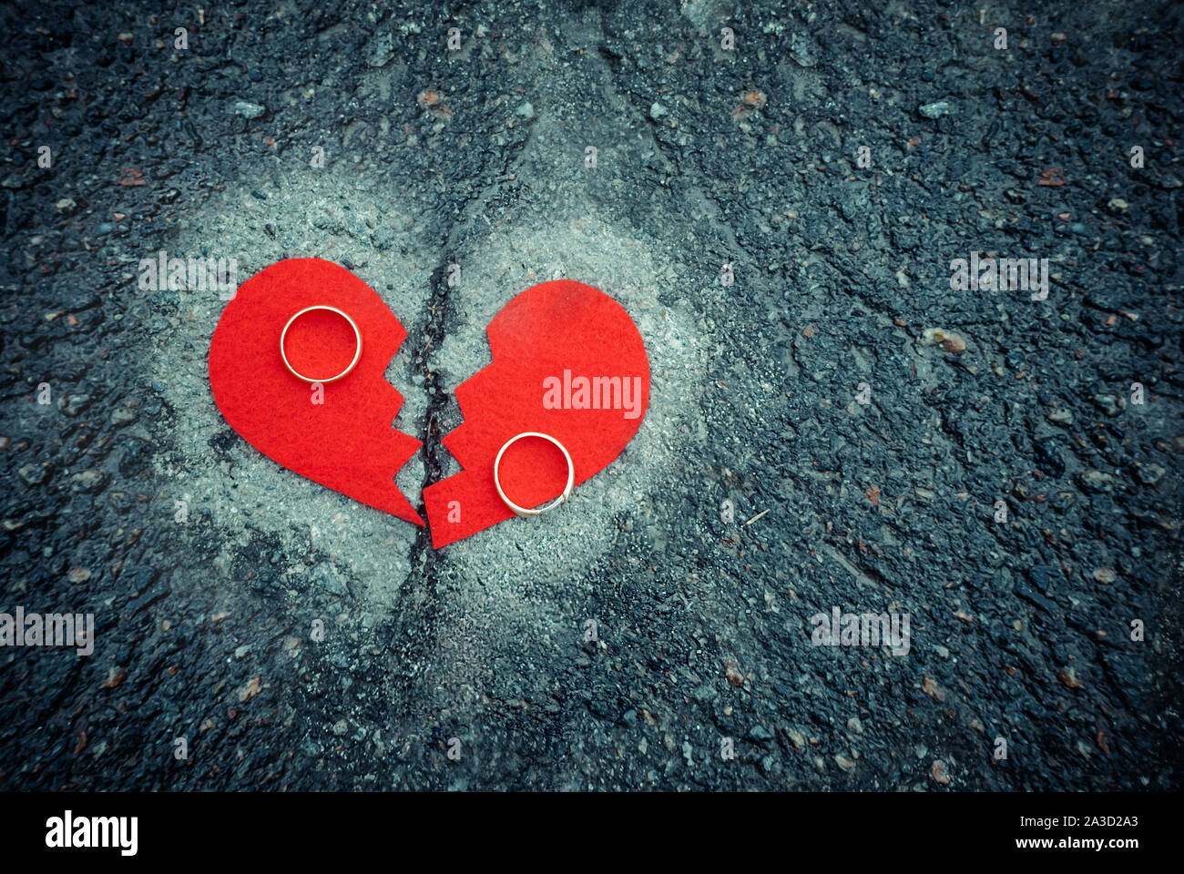 Divorce concept - broken heart with wedding rings on cracked asphalt. Toned Stock Photo