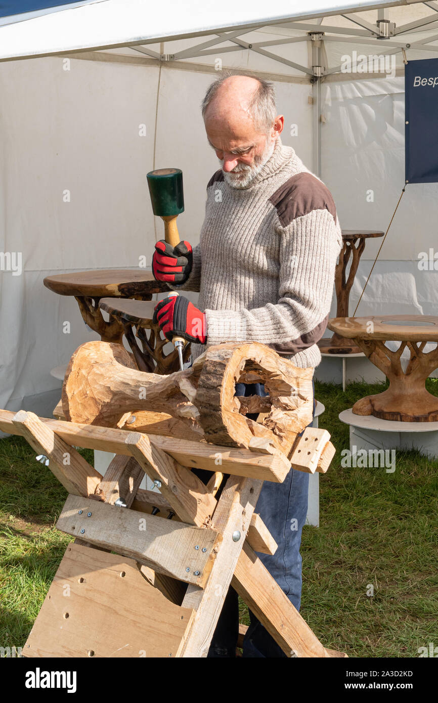 Man demonstrating wood crafts at the Surrey Hills Wood Fair, UK. Artisan carving a bespoke wooden table by hand. Stock Photo