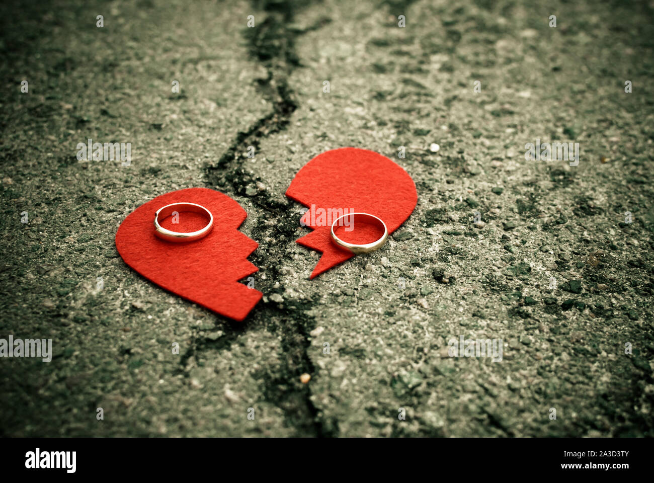 Broken heart with wedding rings on cracked asphalt - divorce concept - Stock Photo