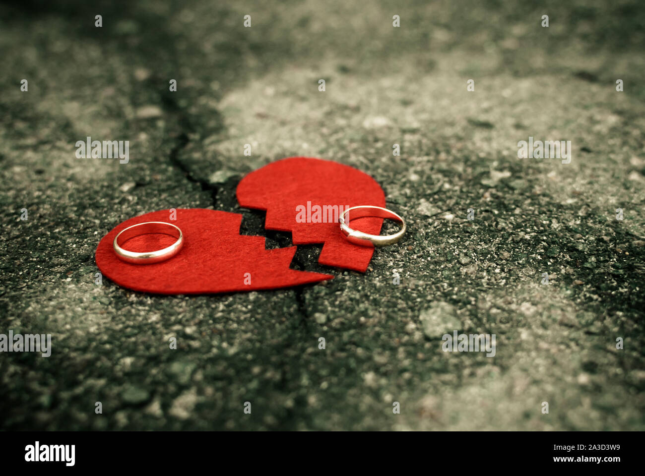 Divorce concept - broken heart with wedding rings on cracked asphalt Stock Photo