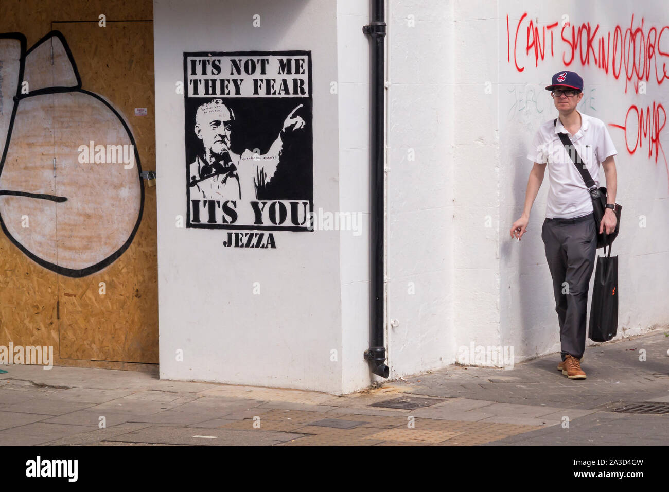m,an walking past jeremy corbyn graffiti Stock Photo