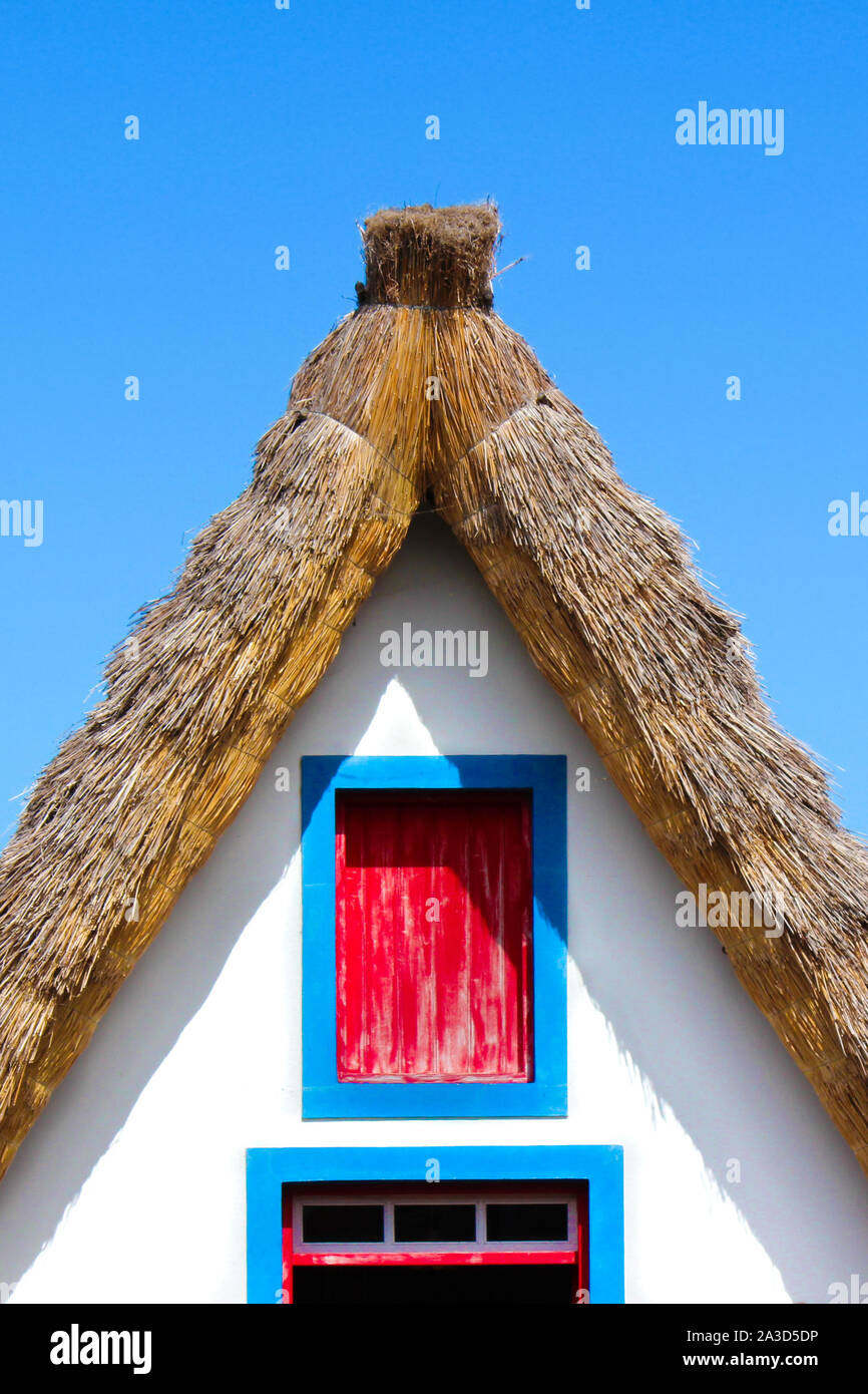 Close up photo of the front side facade of the traditional house in Santana, Madeira Island, Portugal. Typical thatched roof, colorful facade in white, red and blue colors. Portuguese architecture. Stock Photo