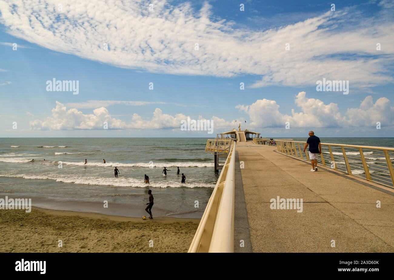A group of African boys playing ball on the seashore near the modern pier of Lido di Camaiore in mid-August day Stock Photo