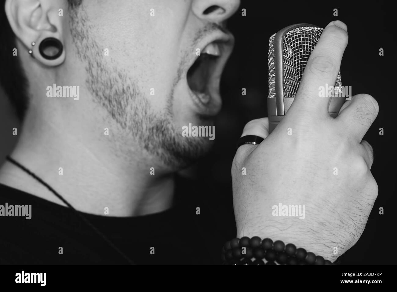 Man screaming on the microphone. Singing heavy metal. Close-up on a man wearing black, holding a studio microphone. Stock Photo