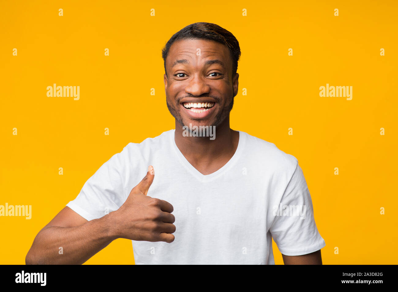 Afro Guy Gesturing Thumbs-Up Smiling At Camera, Yellow Background Stock Photo