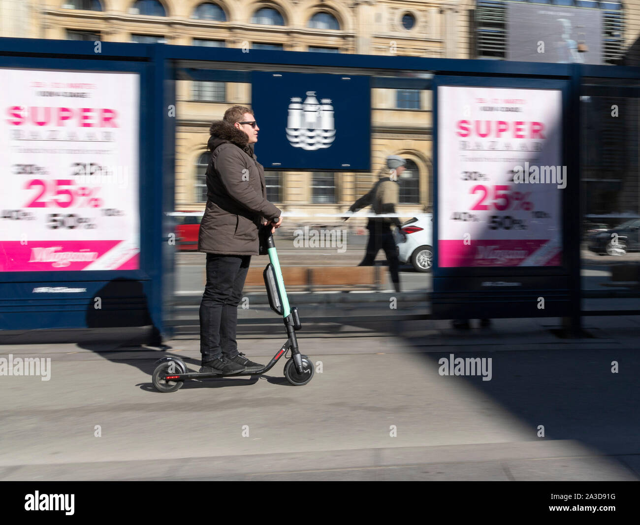 Mann fährt schnell mit E-Roller E-Scooter an Bushaltestelle vorbei Stock Photo