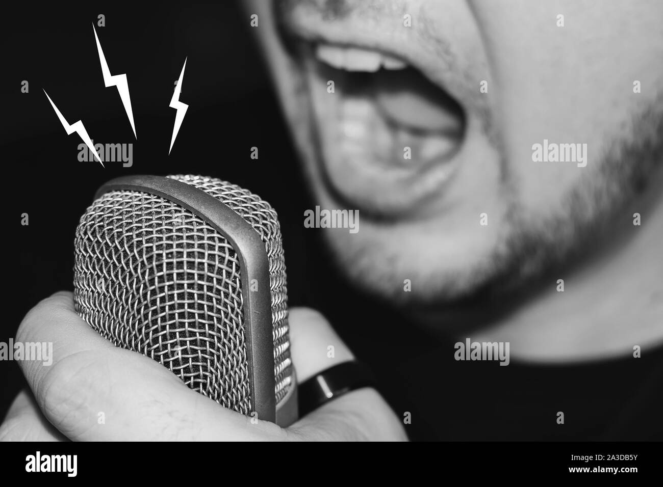 Man screaming on the microphone. Singing heavy metal. Close-up on a man wearing black, holding a studio microphone. Stock Photo