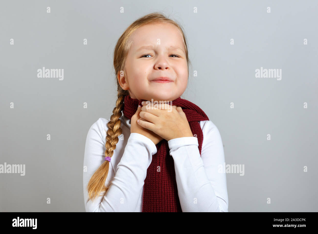 A little girl in a scarf suffers from a sore throat. The child holds on