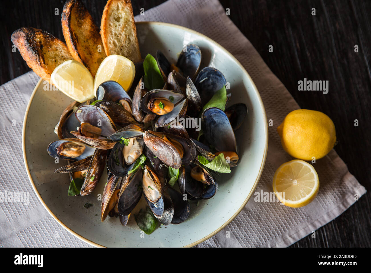 Mussels in clay bowl with lemon on wooden dark background Stock Photo