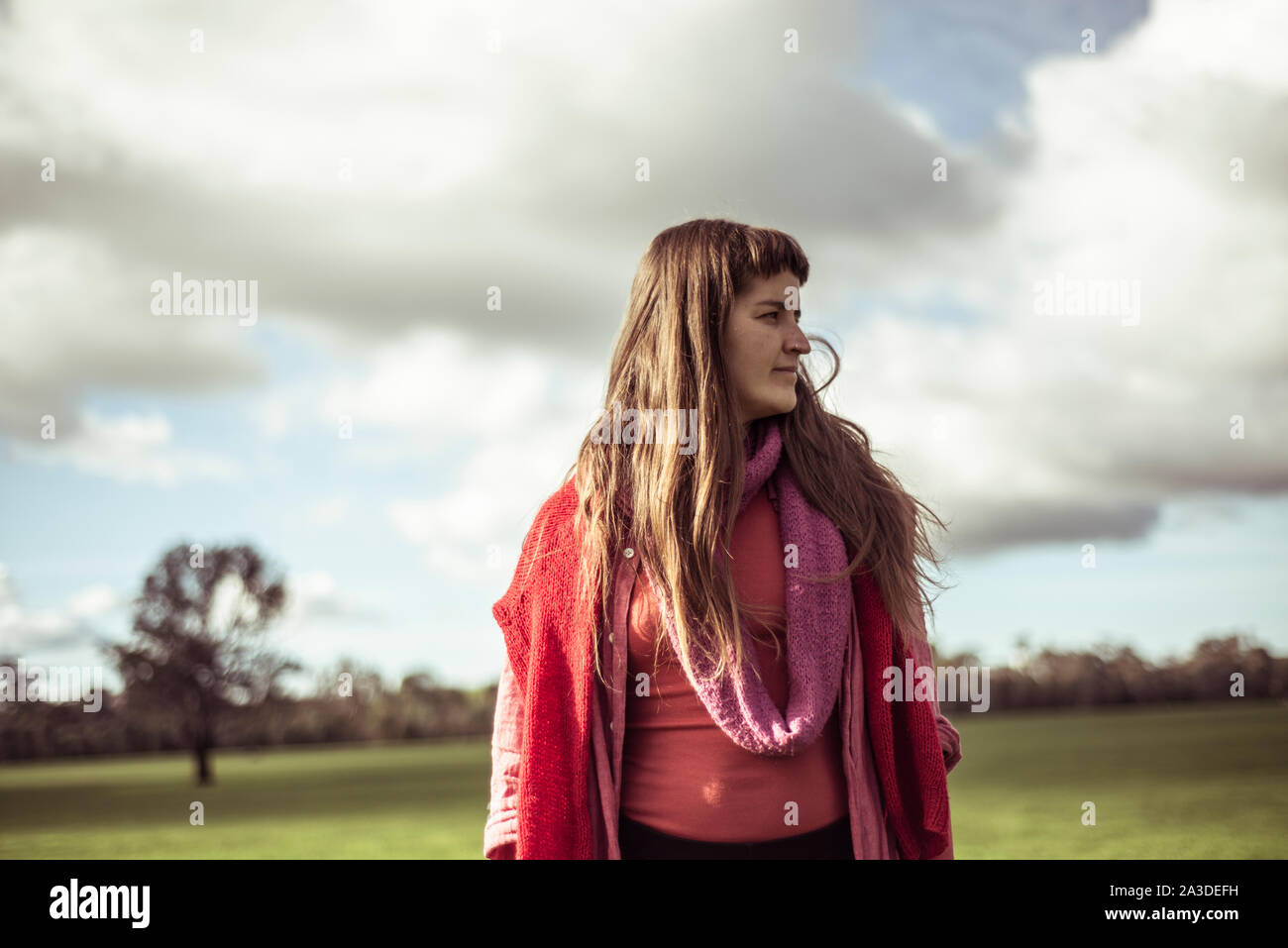 young female farmer stands and looks at green farm land in moody day Stock Photo