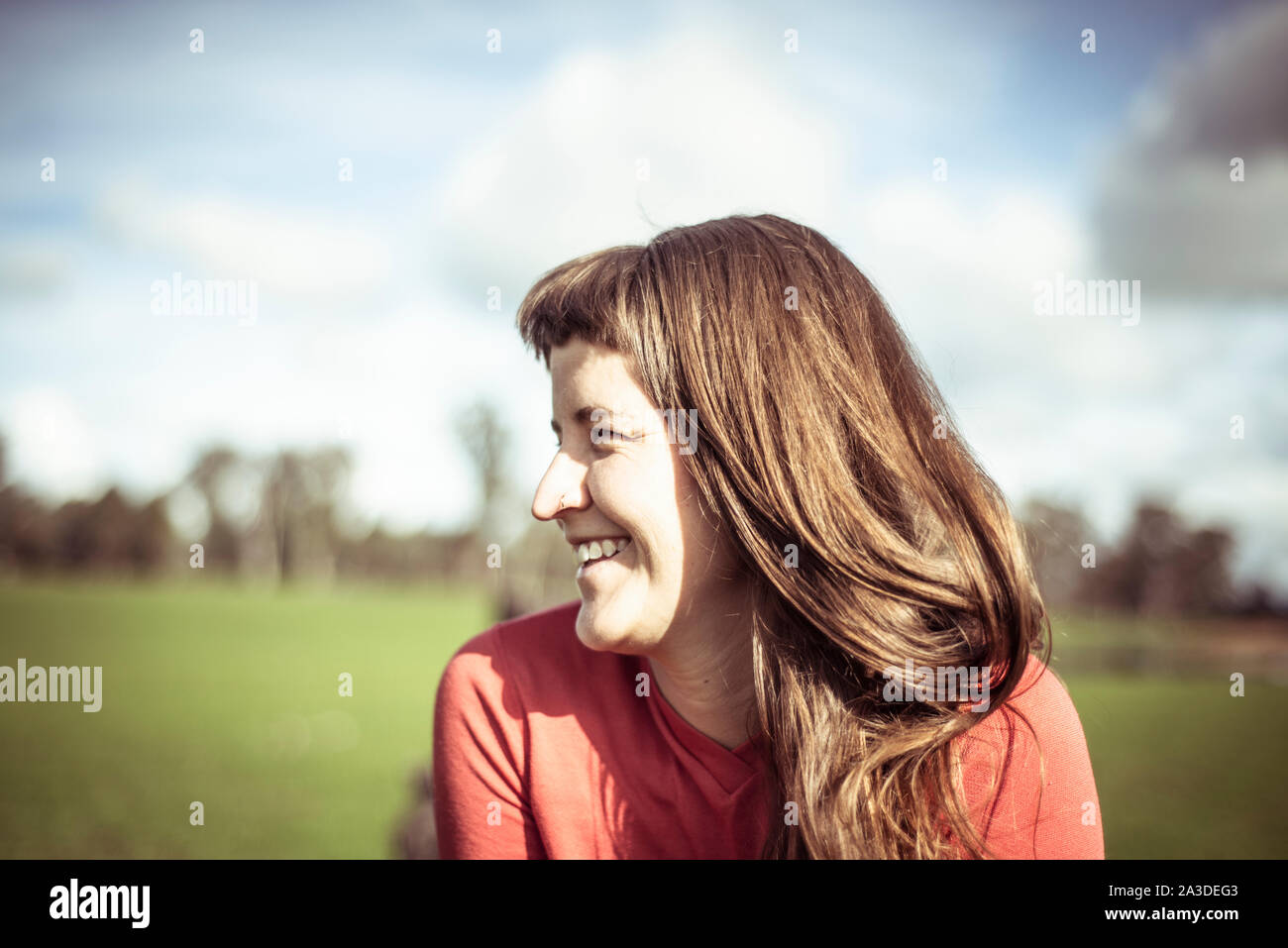 Girl with fringe laughs in sunlight out on green farm land in spring Stock Photo