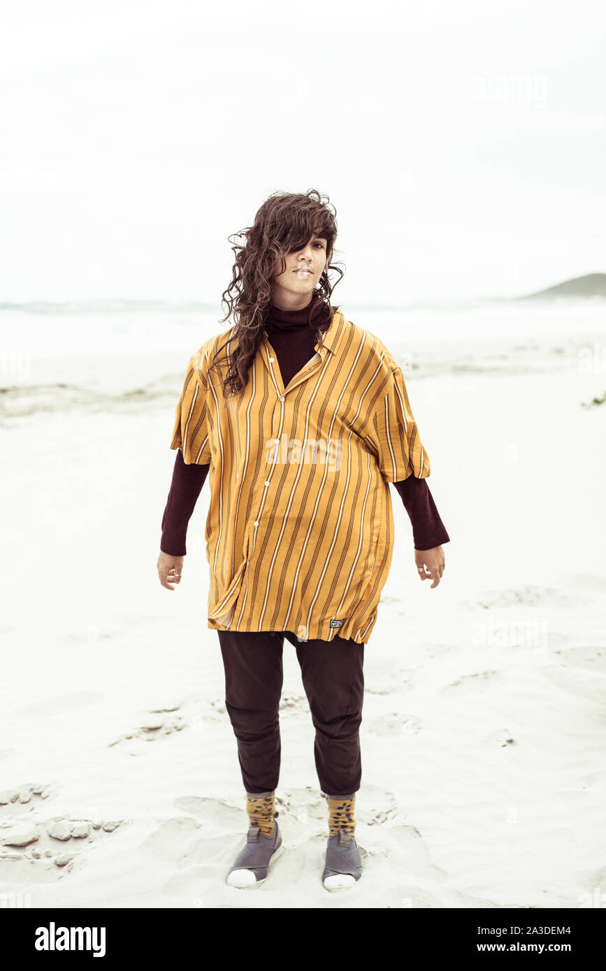 Natural girl stands on windy remote beach with oversized shirt Stock Photo