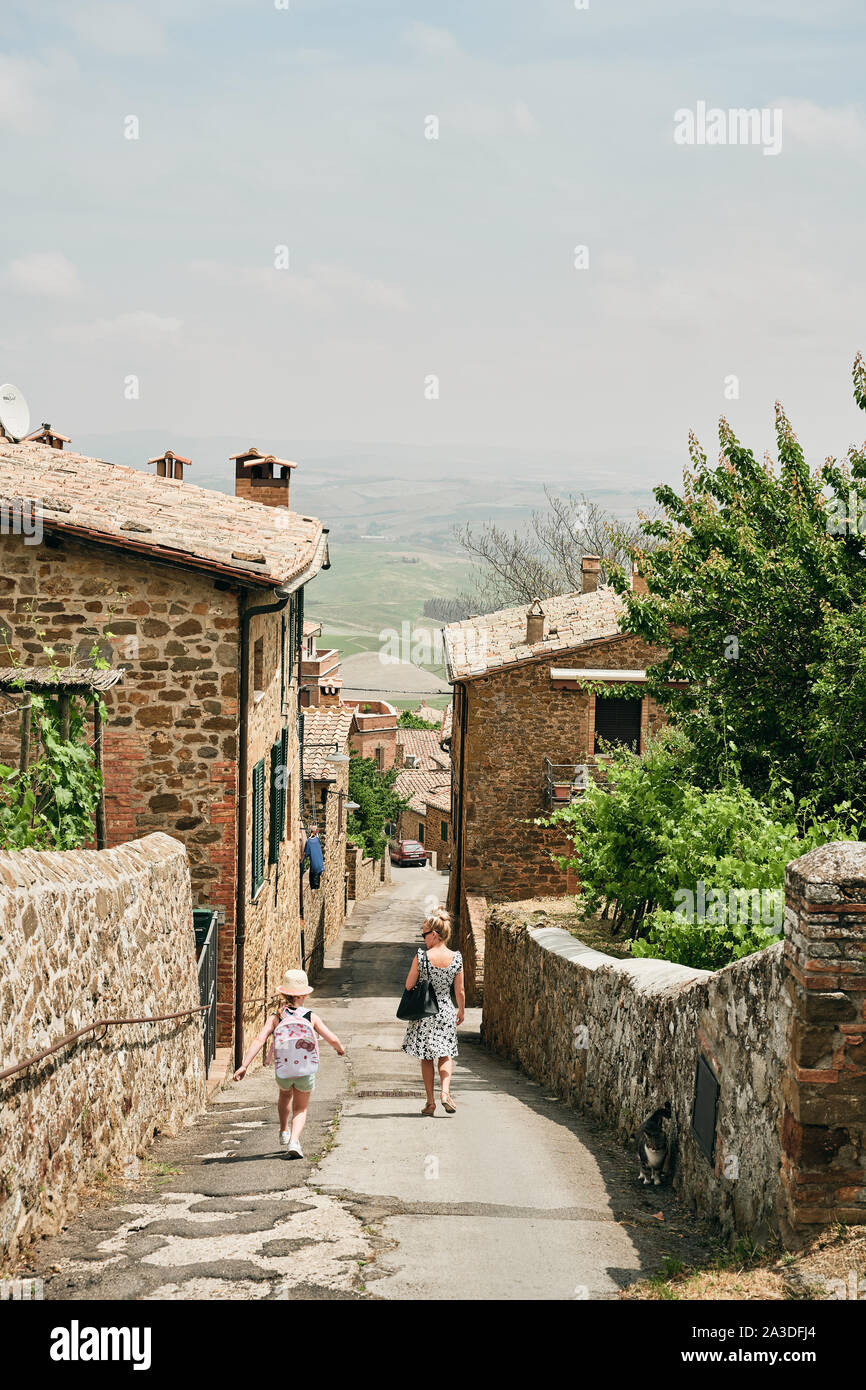 Back view of mother in summer dress walking with daughter down narrow street with bricked charming houses in Tuscany Italy Stock Photo