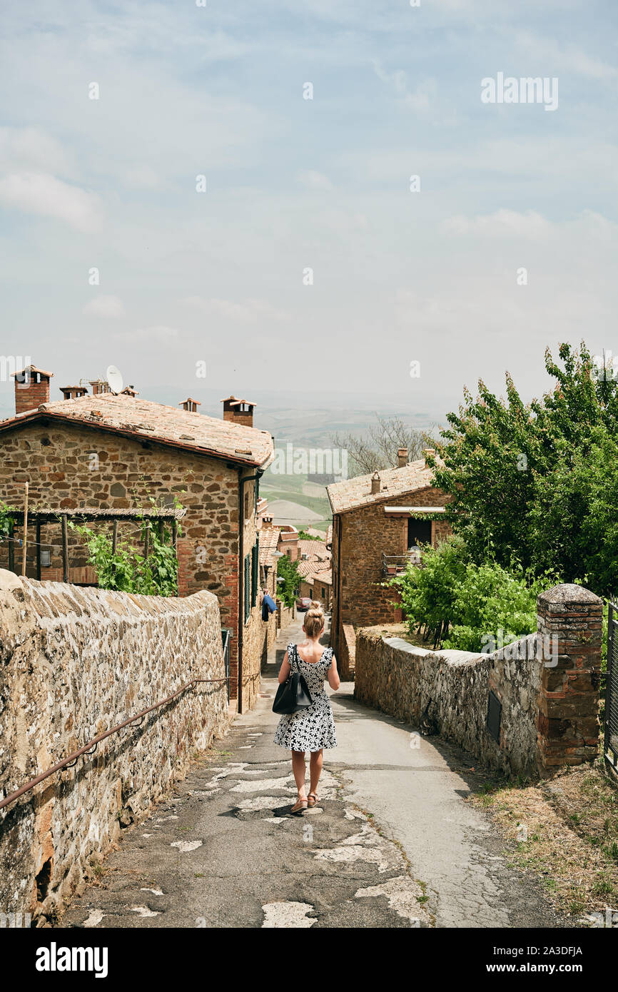 Back view of traveling female in summer dress strolling down narrow street with bricked aged houses in Tuscany Italy Stock Photo