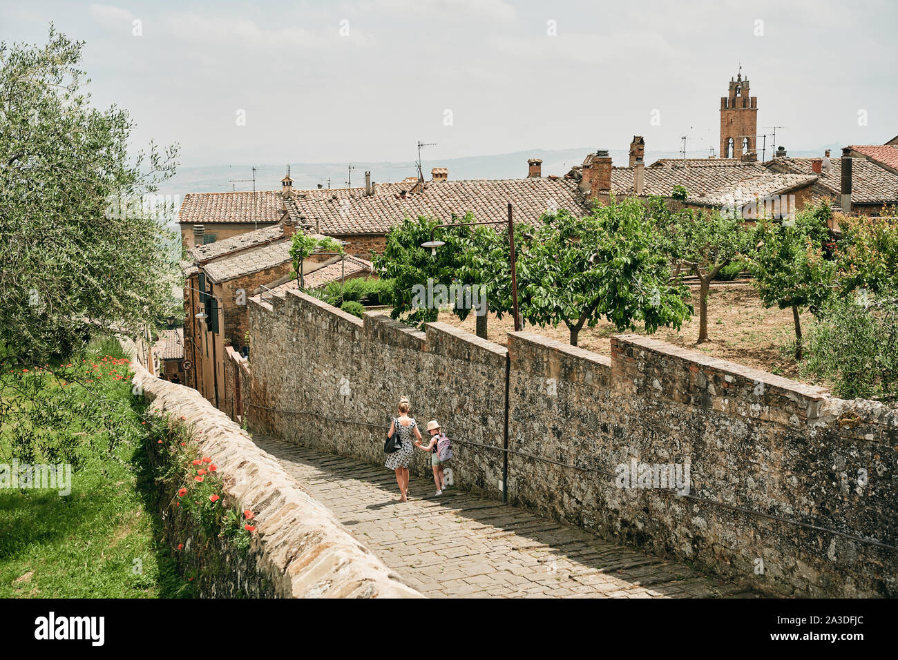 Back view of woman with girl walking down aged tranquil street in old town of Tuscany in Italy Stock Photo