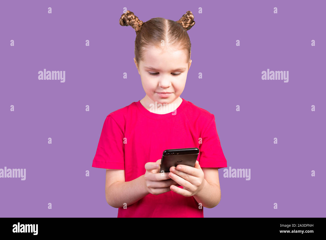 Little girl, in a bright T-shirt, uses a smartphone isolated on a purple background. Stock Photo