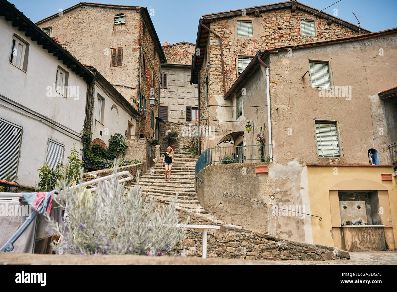 Low angle of traveling woman walking down staircase among brick houses in Tuscany Italy Stock Photo