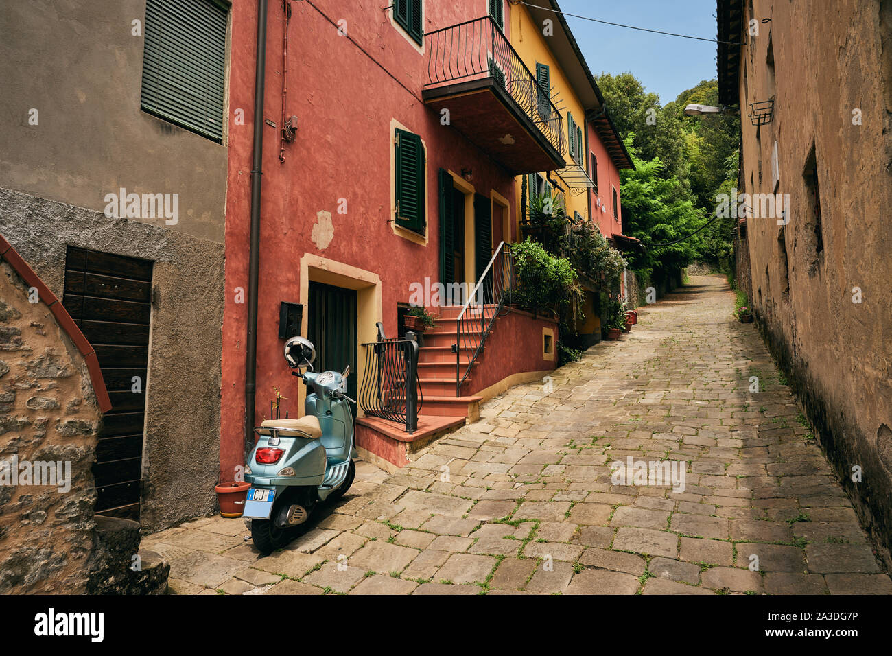 Pedestrian street with scooter parked by bright red house at European town on summer day Stock Photo