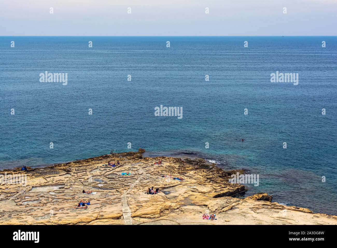 People relaxing on the Silema beach in Malta getting tanned and swimming in Mediterranean Sea. Stock Photo