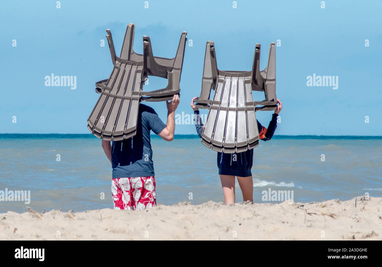 A couple carry plastic beach chairs on their head,moving them closer to the waters of Lake Michigan, so they can coo off Stock Photo