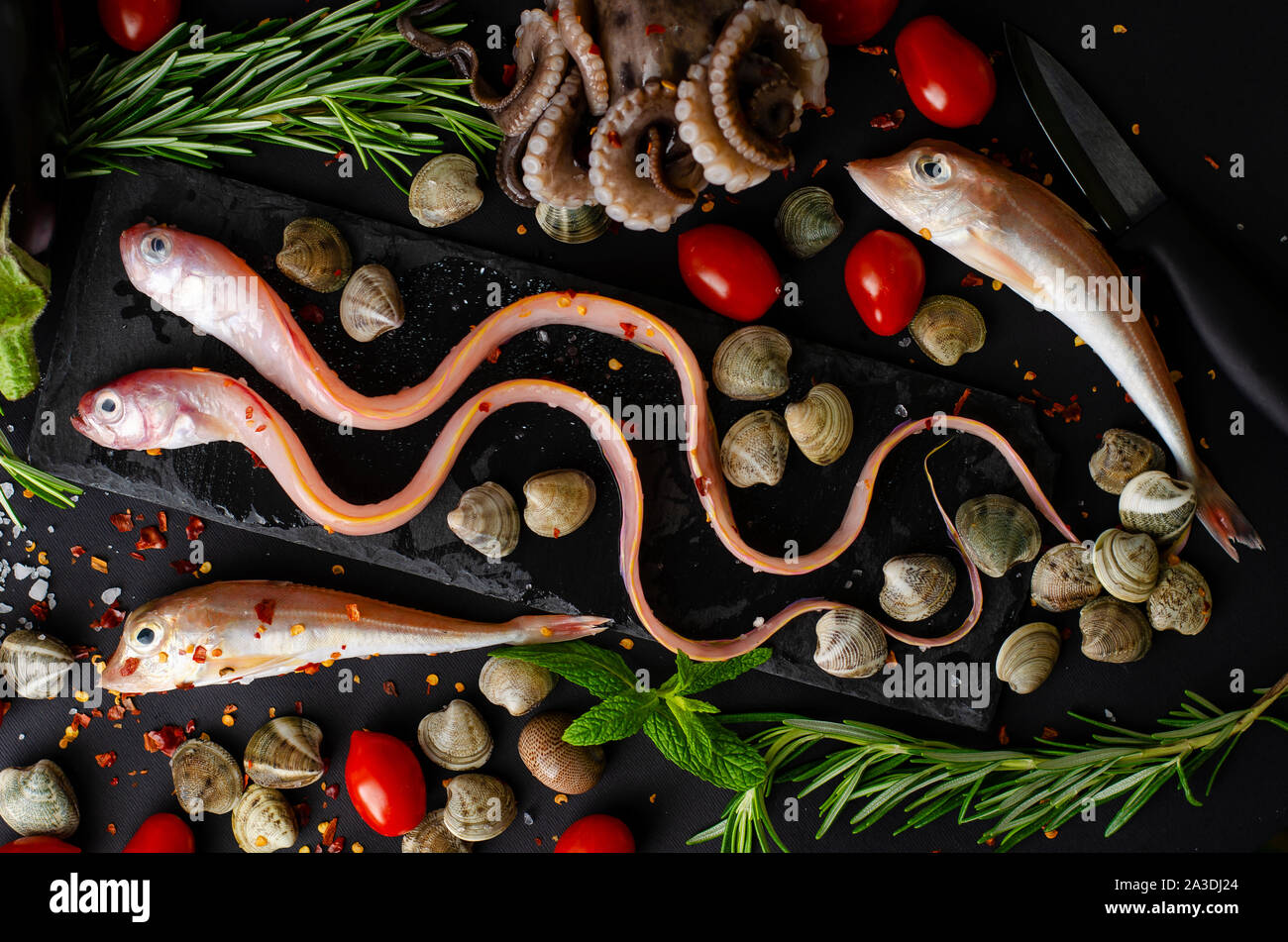 Fresh mixed sea fish, octopus, tomatoes and rosemary on a grill pan on dark bacground. Meditteranean food concept. Top view Stock Photo