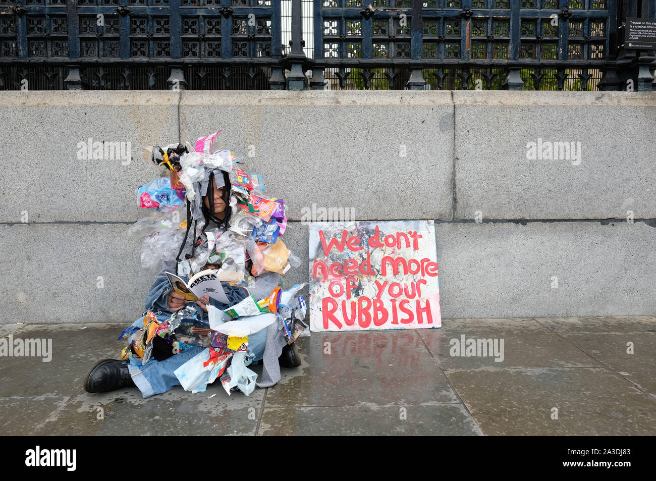 Westminster, London, UK - Monday 7th October 2019 - Extinction Rebellion XR climate protester wearing an outfit made of waste material sits in the rain outside Parliament reading a book about Greta Thunberg on Day 1 of the XR protest. Photo Steven May / Alamy Live News Stock Photo
