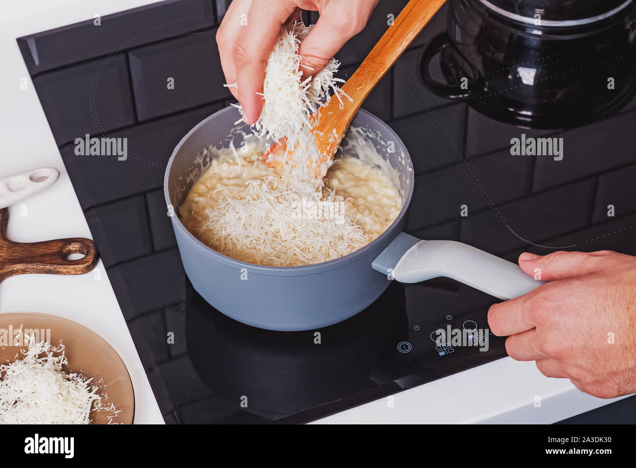Man's hand close-up adding parmesan cheese to the pot with risotto. Stock Photo