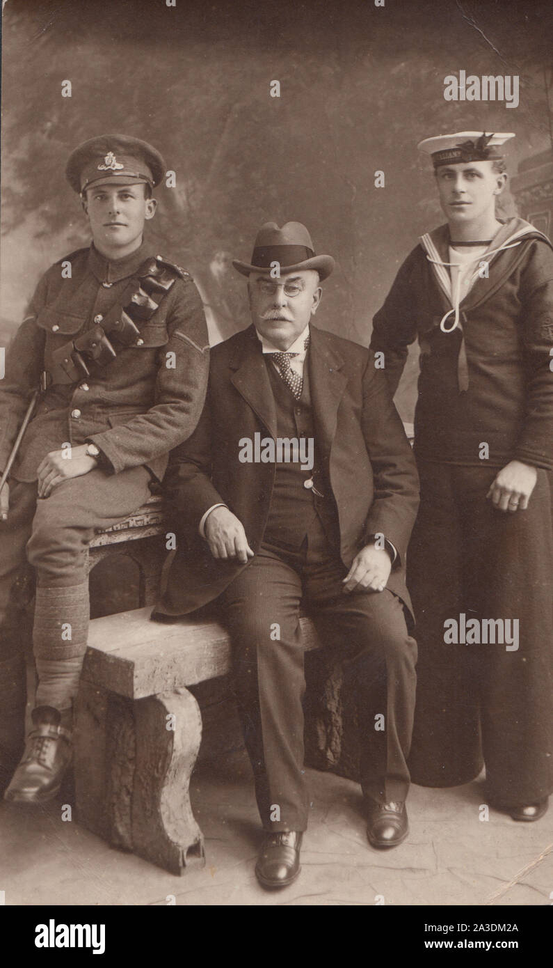 Vintage Early 20th Century Photographic Postcard Showing a Father With His Two Sons. One a British Army Soldier From The Royal Artillery. The Other Son a British Navy Sailor From H.M.S.Valient. Stock Photo