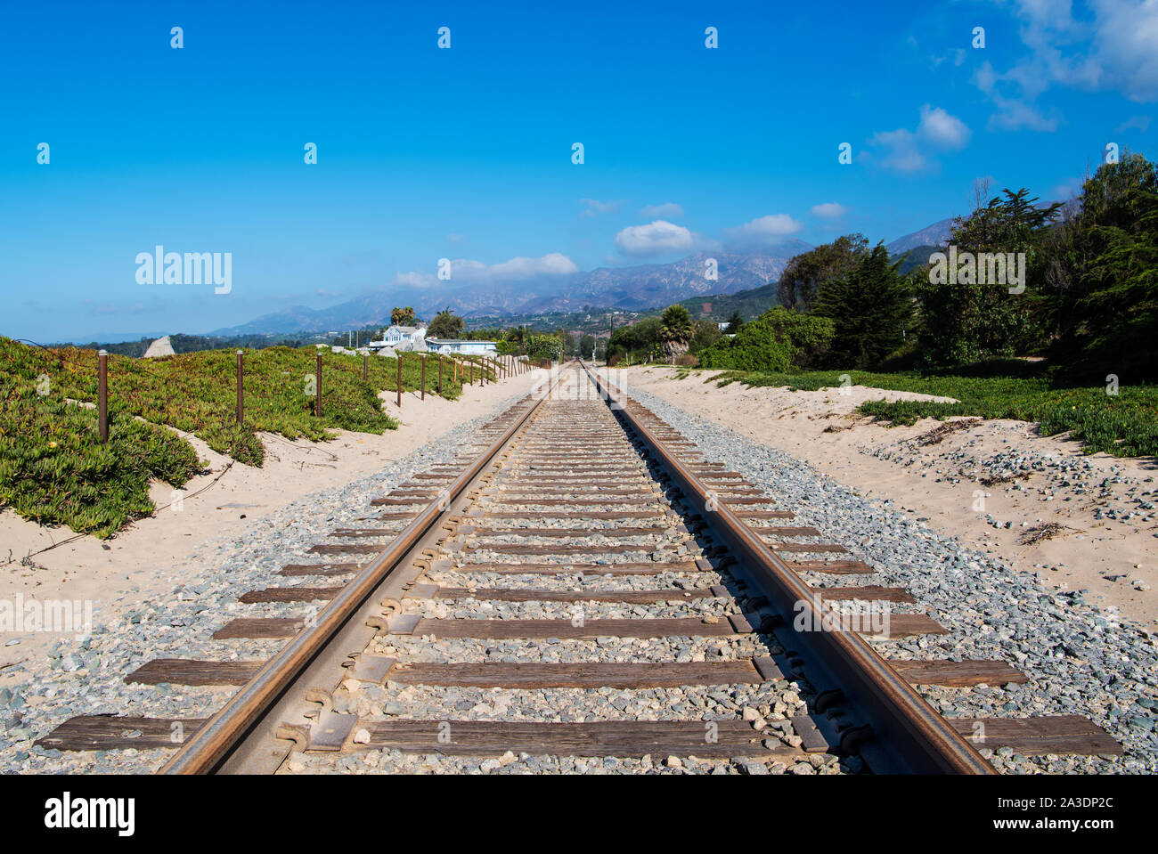 Railroad tracks through sandy dunes covered in green ice plant along California's coastal passenger train route in Santa Barbara Stock Photo