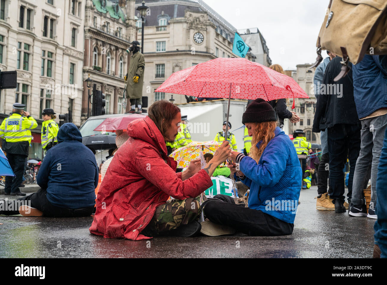 7th Oct 2019 - London, UK. A protesters share an umbrella while blocking the road during Extinction Rebellion climate protest in London. Stock Photo