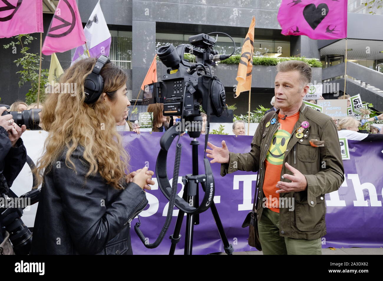 Naturalist and TV presenter Chris Packham heads up a demo outside the HQ of Network Rail, Euston, to prevent the destruction of ancient woodlands along the new proposed HS2 rail link between London, Birmingham, Manchester and Leeds. These include South Cubbington Woods in Warwickshire, which is well know its bluebells, biodiversity and public walks. The banner behind him says 'Tell The Truth' one of Extinction Rebellion's demands. One protester holds a poster saying 'Stop Ecocide'. Chris Packham was also recorded talking for TV. A young protester joined him in sharing a handful of Acorns. Stock Photo
