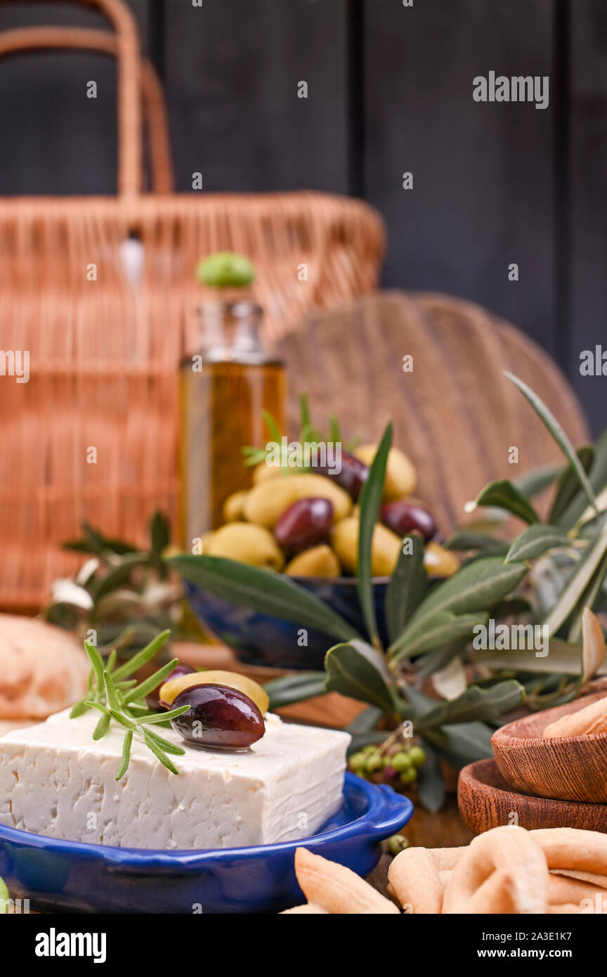 Greek cheese feta with thyme and olives, selective focus. Bread and young olives branch on olive board over old wood background. Overhead view Stock Photo
