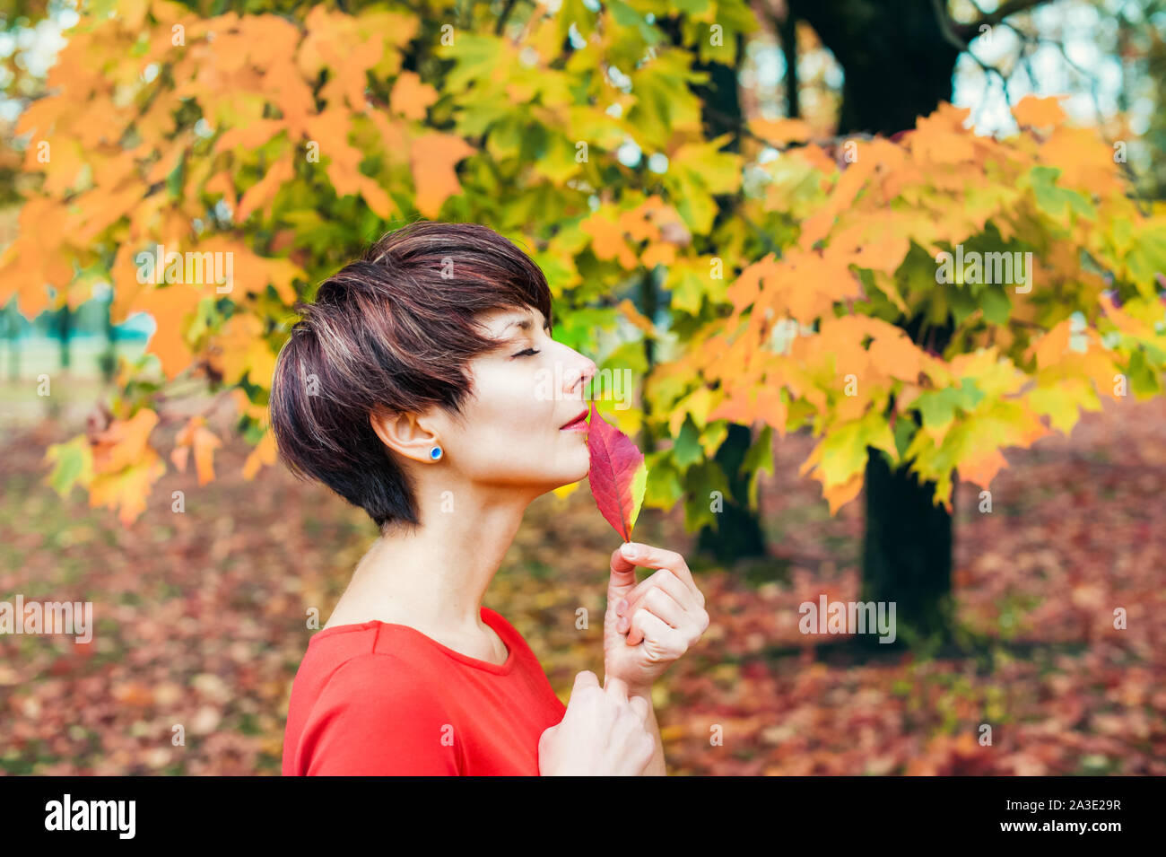 Autumn romantic Beauty. Portrait of Cute Woman in red dress with Fall Leaves in the Park Outdoors in Sunny Day. Seasonal dreamy mood. Copy space Stock Photo
