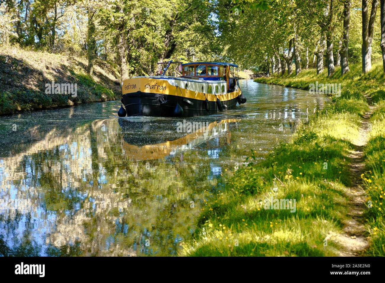 Flat boat navigating a Tree lined bend on the Canal du Midi in south of France. The sycamores perfectly reflected in water Stock Photo