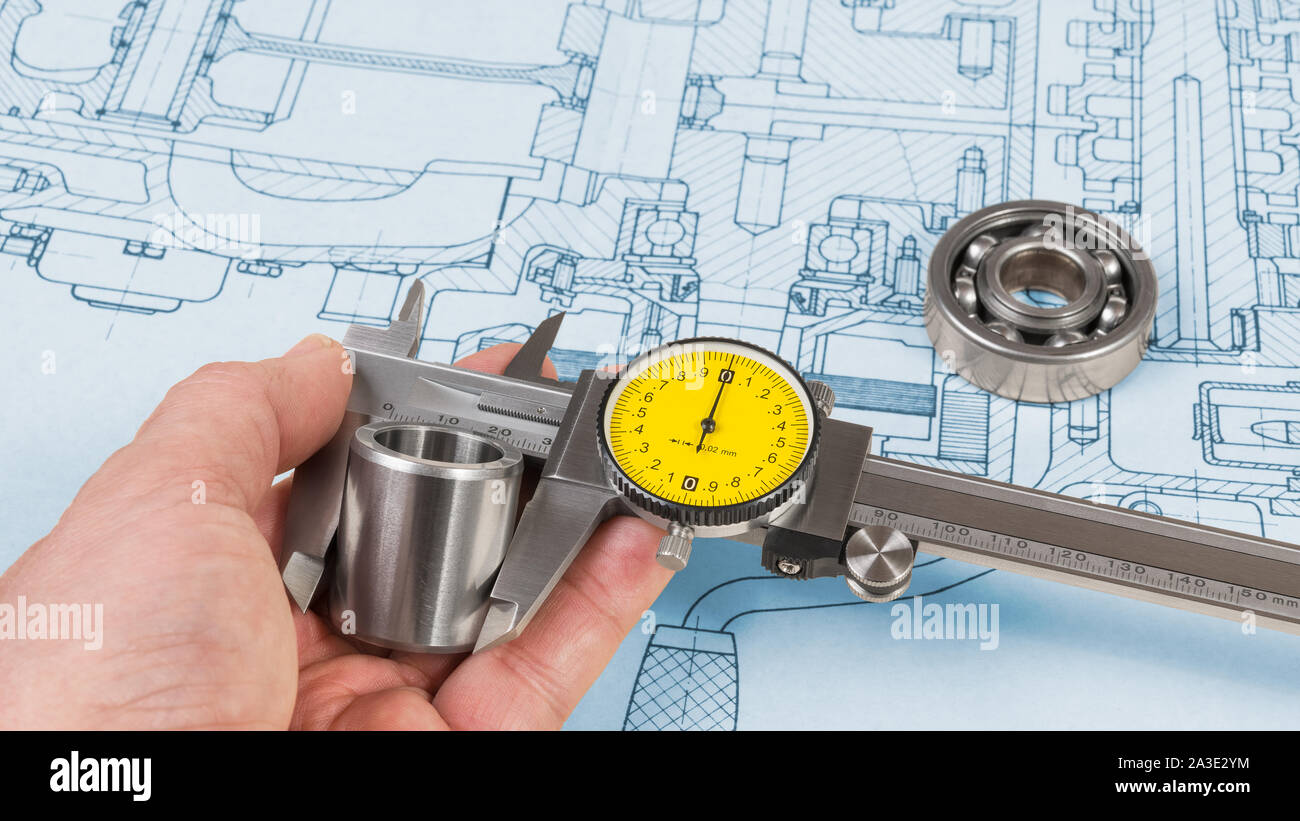 Steel part measurement by caliper in human hand. Ball bearing on technical drawing of combustion engine. Quality control. Engineer with precise tool. Stock Photo