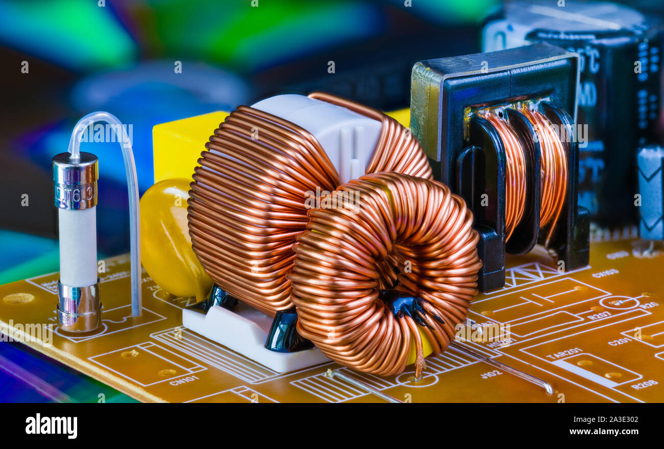 Toroidal inductors with copper wire winding, transformer and electric fuse. Electronic components on circuit board. Dismantled power supply box detail. Stock Photo